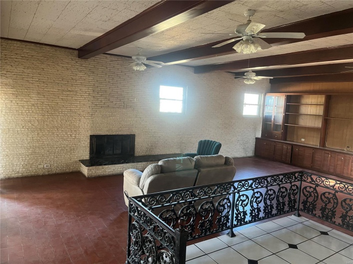 Living area with a brick fireplace, beam ceiling, brick floor, brick wall, and a ceiling fan