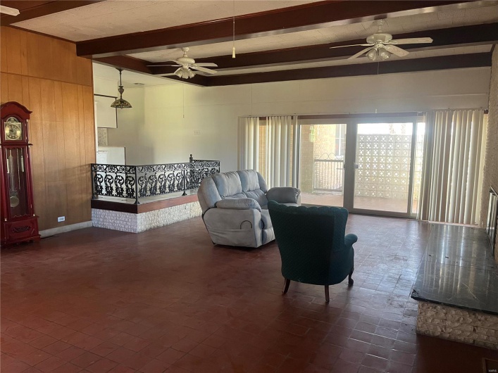 Living area with beamed ceiling, wooden walls, ceiling fan, and brick floor