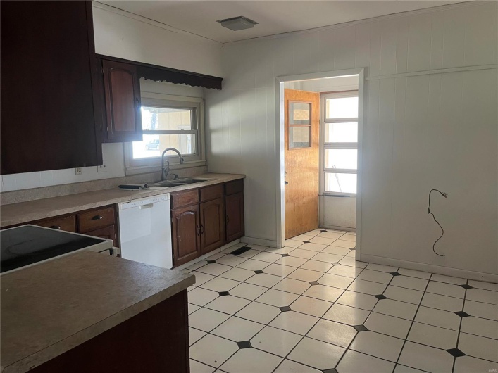 Kitchen featuring light countertops, white appliances, dark brown cabinets, light floors, and a sink