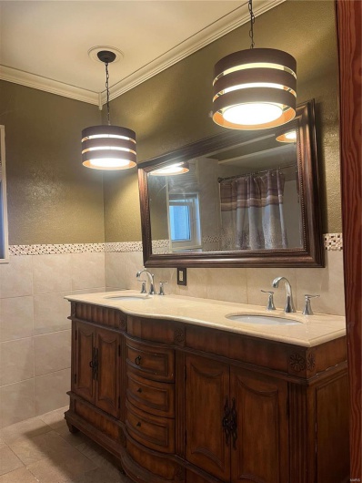 Full bath with tile walls, double vanity, ornamental molding, and a sink