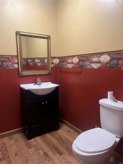 Half bath with toilet, vanity, baseboards, and wood finished floors