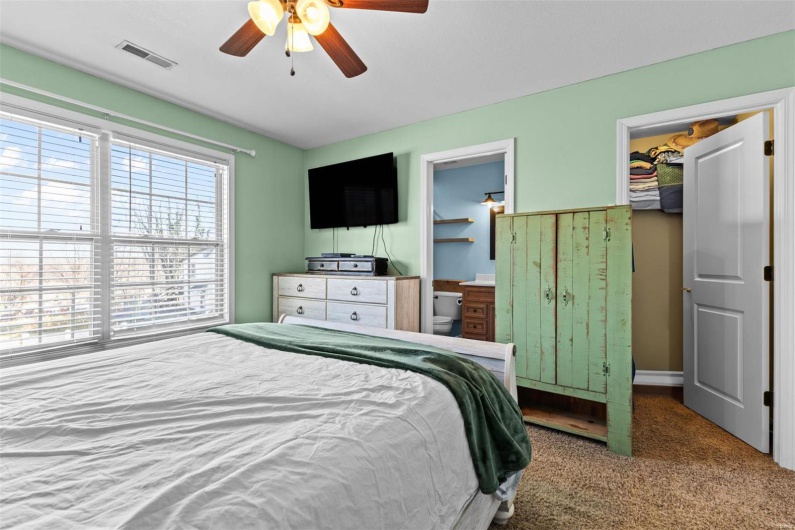 Carpeted bedroom featuring a walk in closet, ensuite bath, and ceiling fan