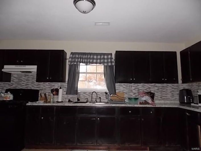 Kitchen with sink, backsplash, black range oven, and exhaust hood