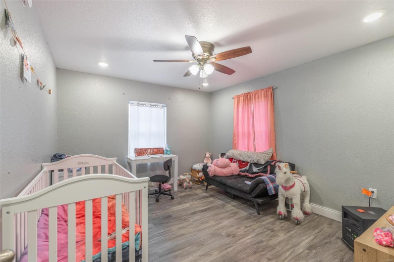 Bedroom featuring ceiling fan, a nursery area, and wood-type flooring