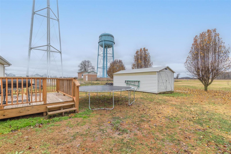 View of yard featuring a trampoline, a deck, and a storage shed