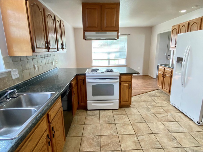 Kitchen with dark countertops, white appliances, under cabinet range hood, tasteful backsplash, and a sink