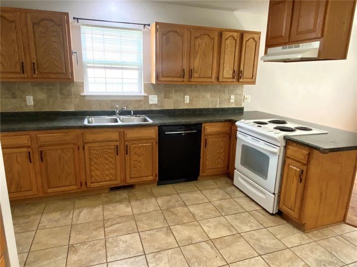 Kitchen featuring white electric range oven, a sink, black dishwasher, tasteful backsplash, and under cabinet range hood