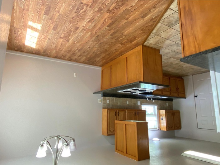 Kitchen with dark countertops, a chandelier, a peninsula, backsplash, and stovetop