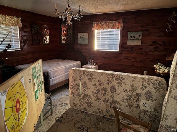 Bedroom featuring a chandelier, a textured ceiling, and wood walls