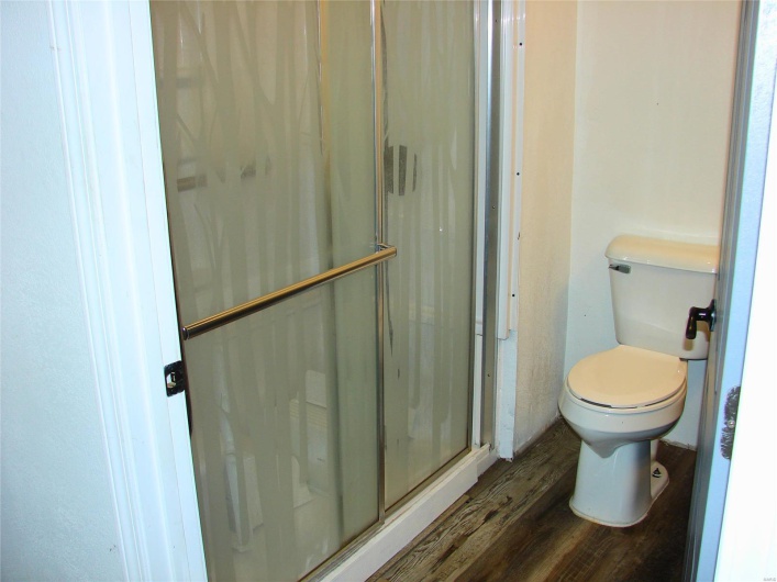 Bathroom with wood-type flooring, toilet, and a shower with door