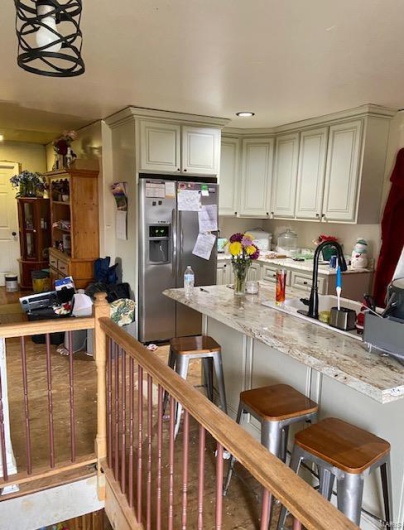 Kitchen featuring stainless steel refrigerator with ice dispenser, light stone counters, sink, wood-type flooring, and a breakfast bar area