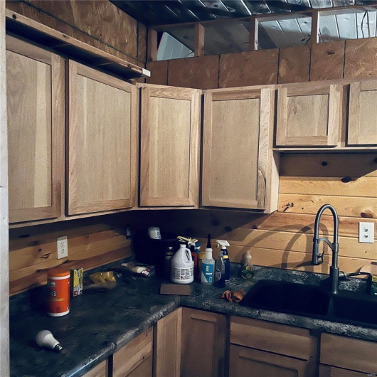 Kitchen featuring light brown cabinetry, wood walls, sink, and dark stone counters