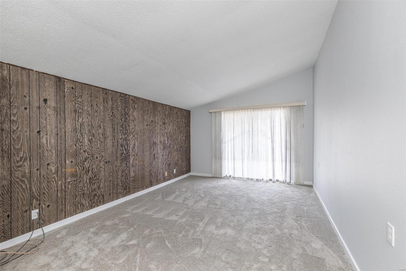 Carpeted empty room with lofted ceiling, a textured ceiling, and wooden walls