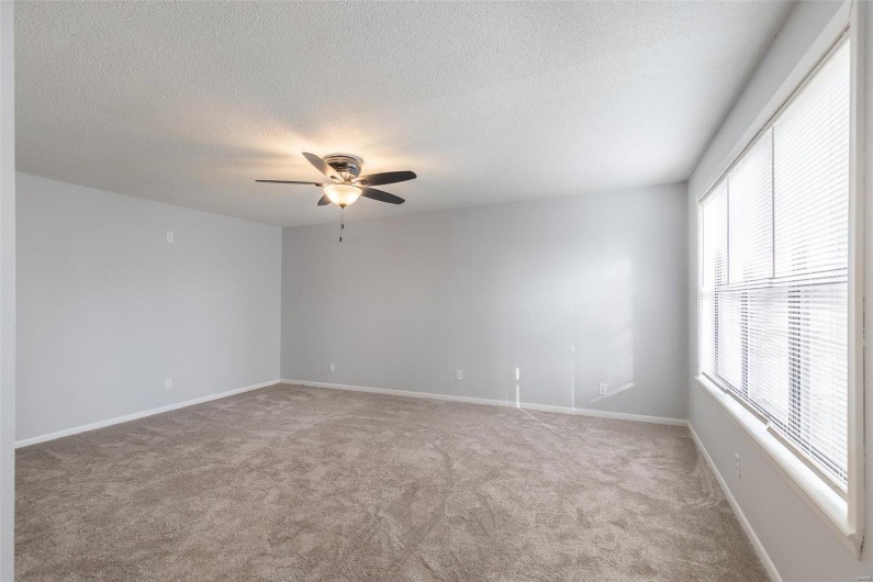 Carpeted spare room featuring plenty of natural light and ceiling fan