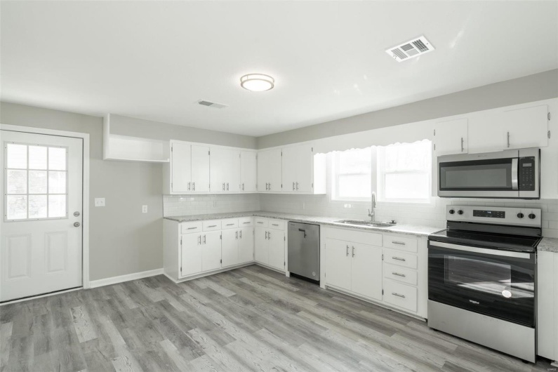 Kitchen with decorative backsplash, appliances with stainless steel finishes, sink, white cabinets, and light hardwood / wood-style floors