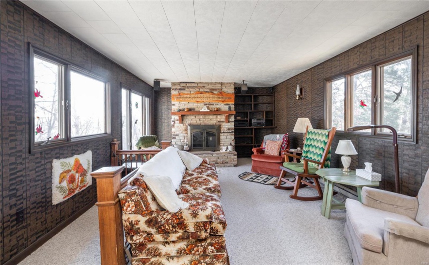 Carpeted living room with plenty of natural light, a fireplace, and brick wall