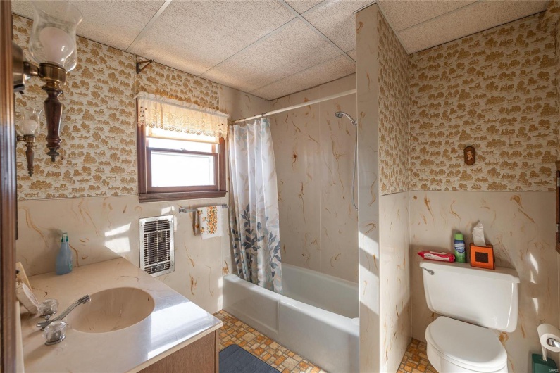 Full bathroom with a drop ceiling, toilet, shower / bathtub combination with curtain, and sink
