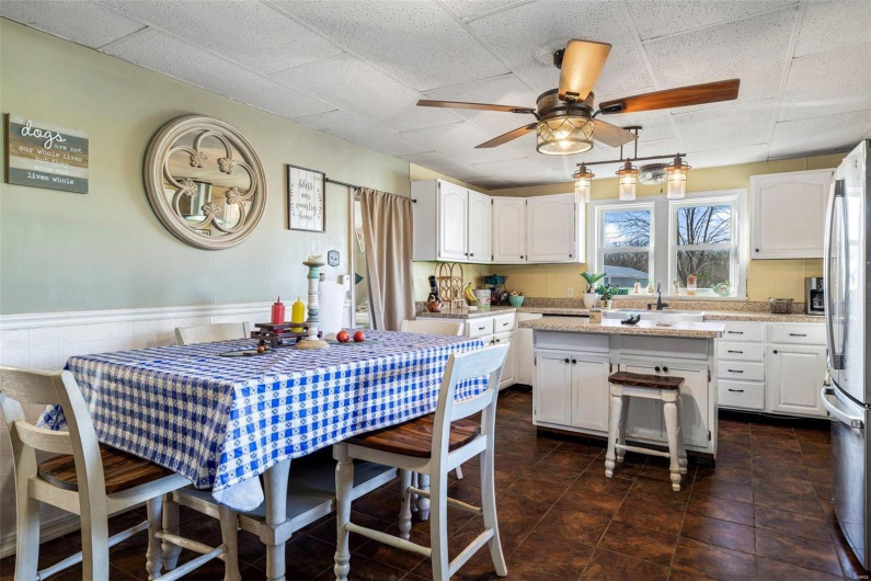 Kitchen featuring ceiling fan, a kitchen island, light stone counters, white cabinetry, and stainless steel refrigerator
