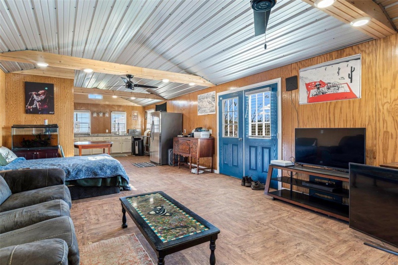 Living room featuring vaulted ceiling with beams, ceiling fan, and wooden walls