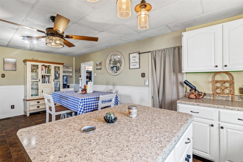 Kitchen featuring a paneled ceiling, ceiling fan, white cabinets, and a kitchen island