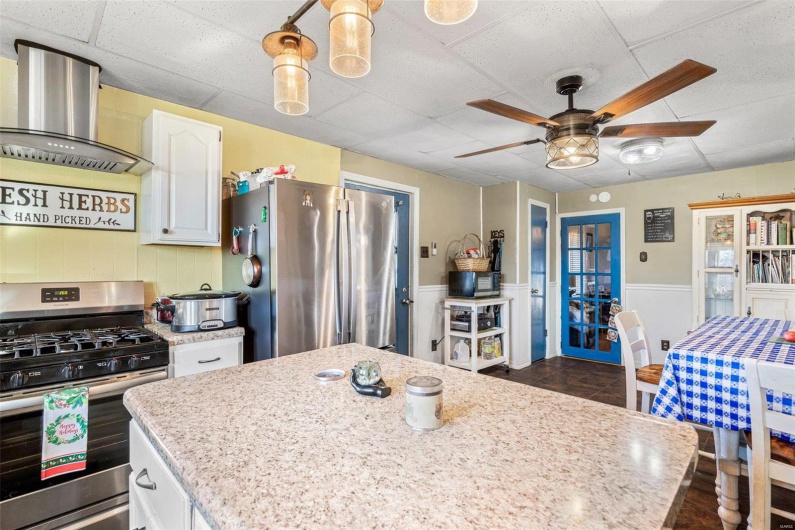 Kitchen with white cabinets, appliances with stainless steel finishes, pendant lighting, and wall chimney exhaust hood