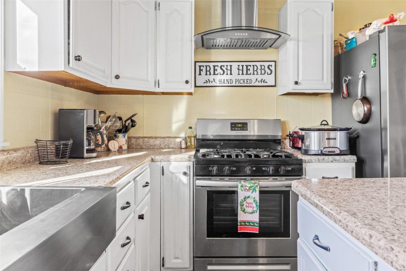 Kitchen with white cabinetry, wall chimney range hood, appliances with stainless steel finishes, and tasteful backsplash