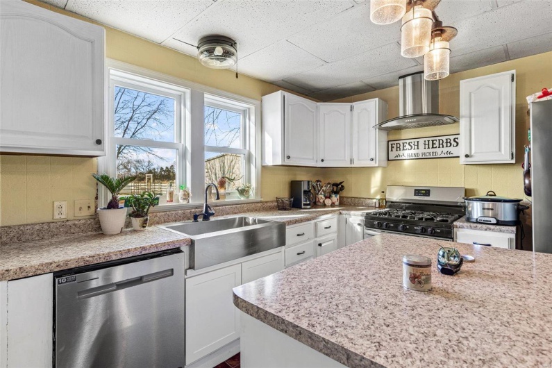 Kitchen featuring pendant lighting, white cabinets, sink, wall chimney exhaust hood, and stainless steel appliances