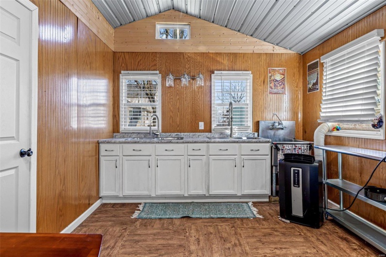 Kitchen with white cabinets, lofted ceiling, wood walls, and sink