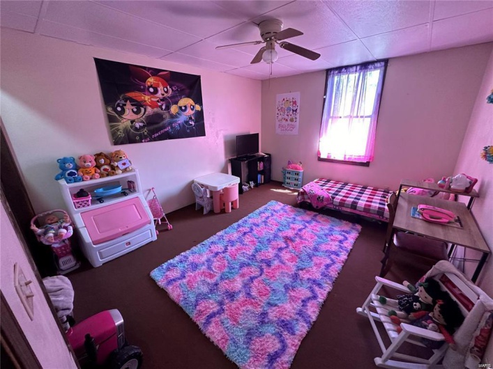 Playroom with dark colored carpet, a drop ceiling, and ceiling fan