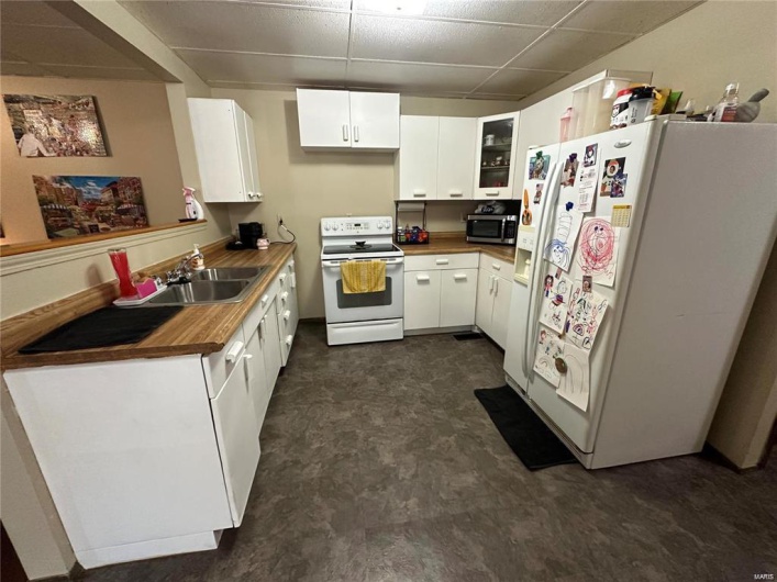 Kitchen featuring a paneled ceiling, white cabinetry, white appliances, and sink