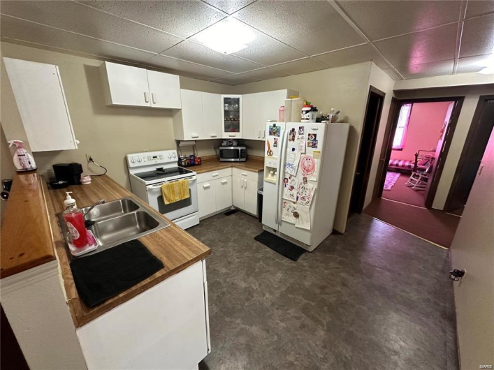 Kitchen featuring a drop ceiling, white cabinetry, white appliances, and sink
