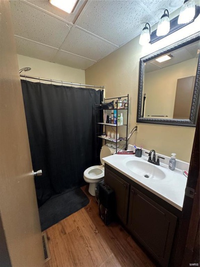 Bathroom with hardwood / wood-style flooring, a drop ceiling, toilet, and vanity