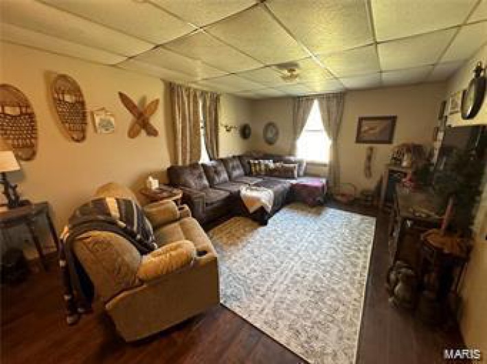 Living room with a paneled ceiling and dark wood-type flooring