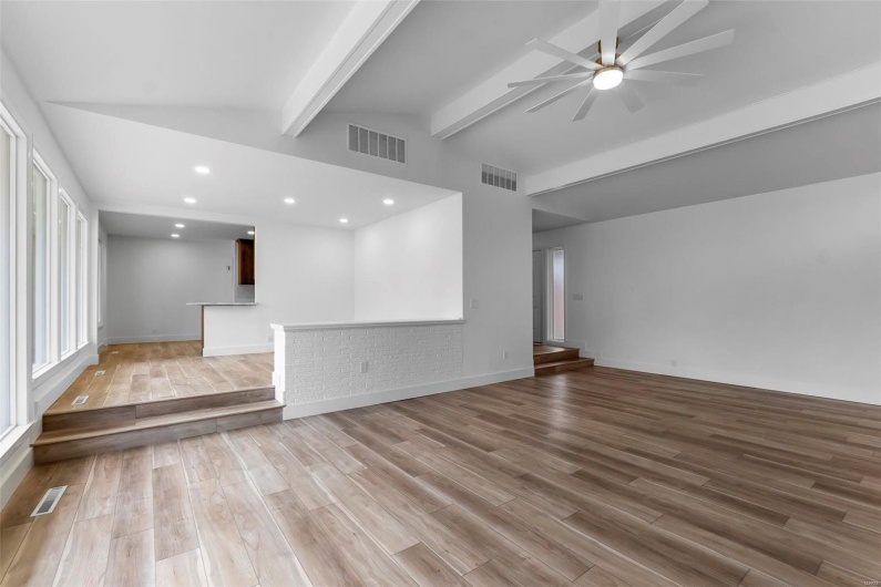 Unfurnished living room featuring vaulted ceiling with beams, ceiling fan, and light hardwood / wood-style flooring