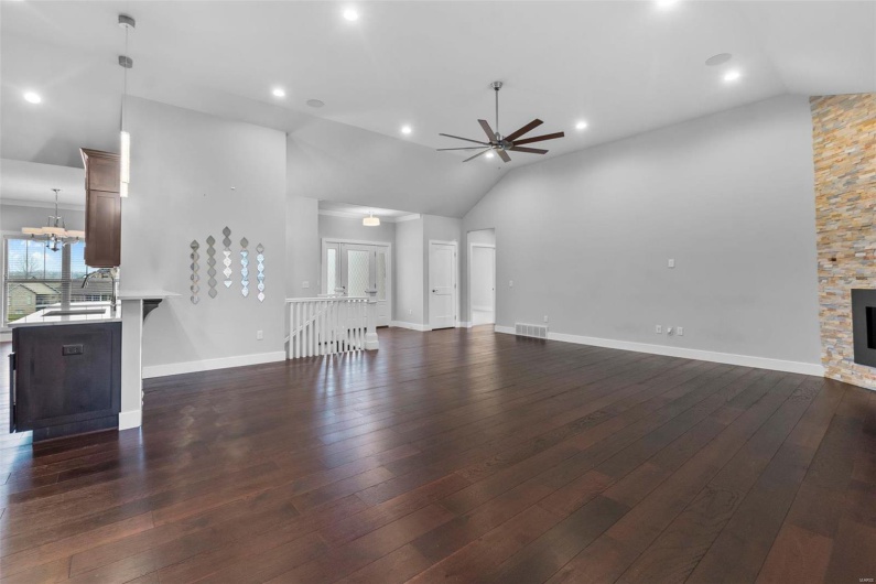 Unfurnished living room featuring ceiling fan with notable chandelier, dark hardwood / wood-style floors, a fireplace, and high vaulted ceiling
