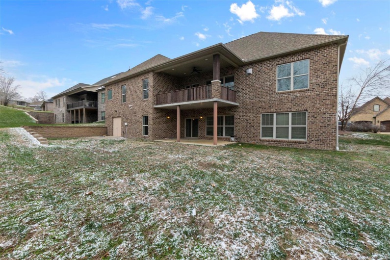 Rear view of house with a balcony, ceiling fan, and a lawn