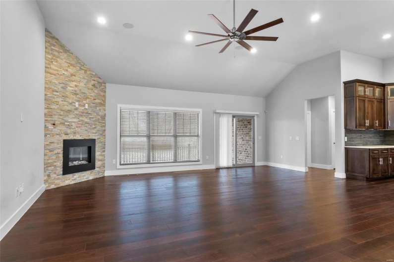 Unfurnished living room with ceiling fan, a stone fireplace, a wealth of natural light, and vaulted ceiling