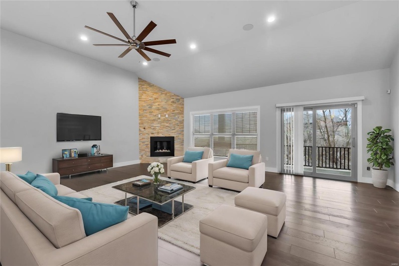 Living room featuring a stone fireplace, ceiling fan, high vaulted ceiling, and wood-type flooring