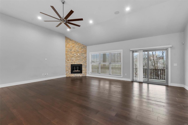 Unfurnished living room featuring dark hardwood / wood-style flooring, high vaulted ceiling, a stone fireplace, and ceiling fan