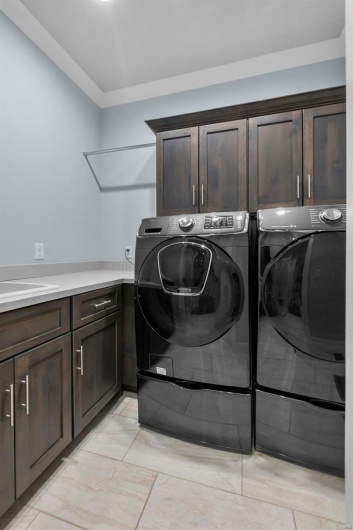 Laundry area featuring separate washer and dryer, light tile patterned floors, and cabinets