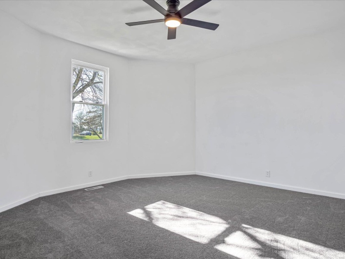Empty room with ceiling fan and dark carpet