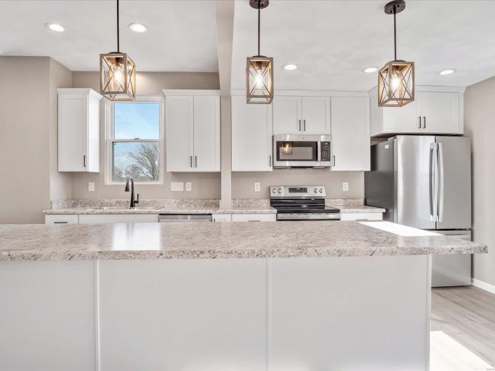 Kitchen with white cabinets, sink, light stone countertops, decorative light fixtures, and stainless steel appliances