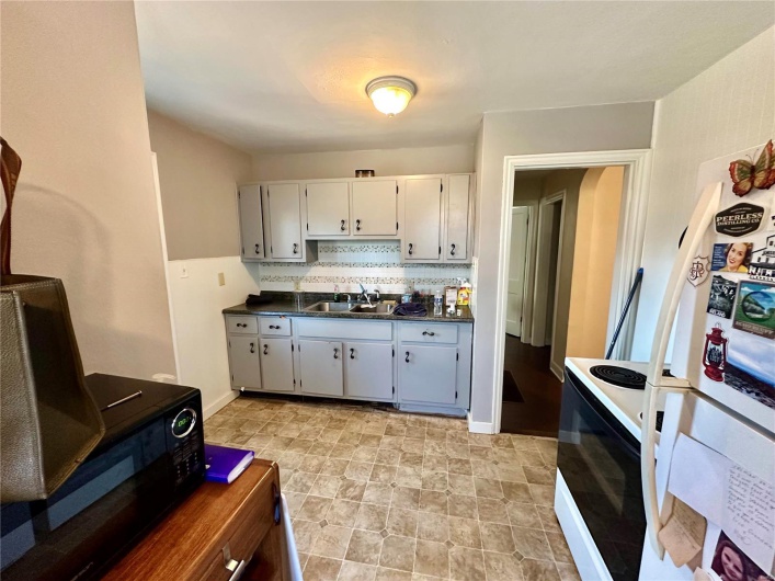 Kitchen with electric range oven, sink, decorative backsplash, white fridge, and white cabinetry