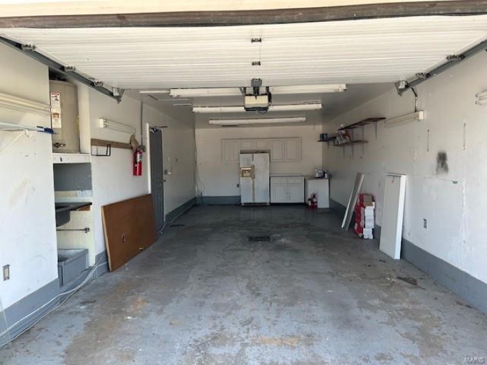 Garage with a garage door opener and white refrigerator with ice dispenser