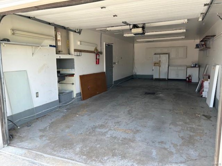 Garage featuring white refrigerator with ice dispenser and a garage door opener