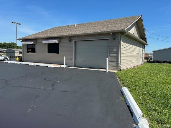 View of property exterior featuring a garage, an AC wall unit, and a lawn