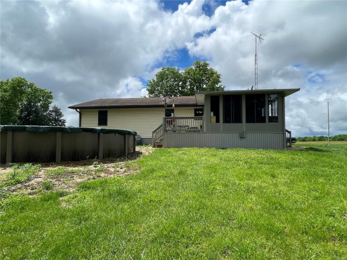 Back of property with a sunroom, a covered pool, a lawn, and a deck