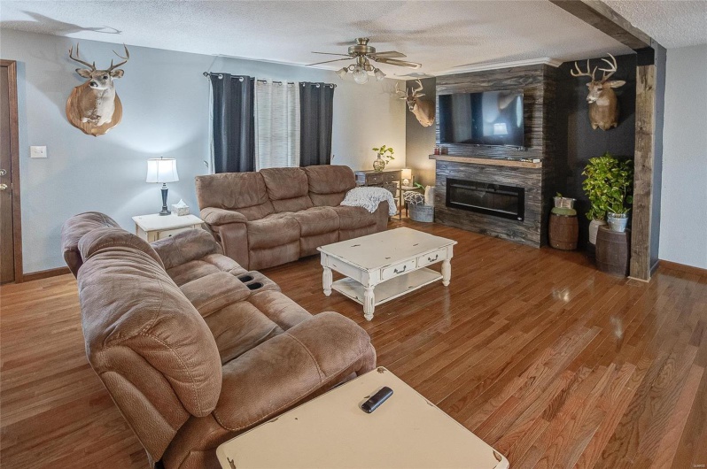 Living room with a large fireplace, a textured ceiling, ceiling fan, and hardwood / wood-style floors