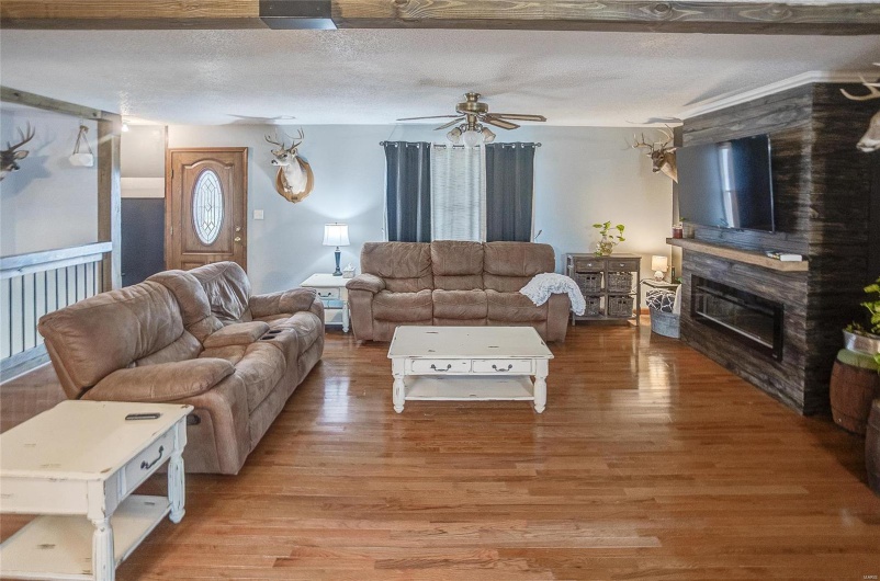 Living room featuring a textured ceiling, light wood-type flooring, ceiling fan, and a fireplace