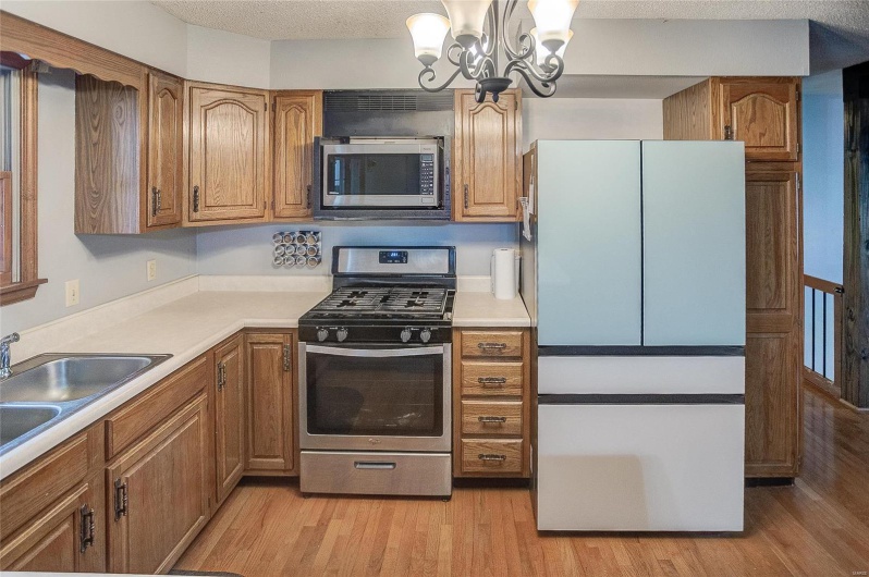 Kitchen featuring stainless steel appliances, light wood-type flooring, a textured ceiling, sink, and an inviting chandelier